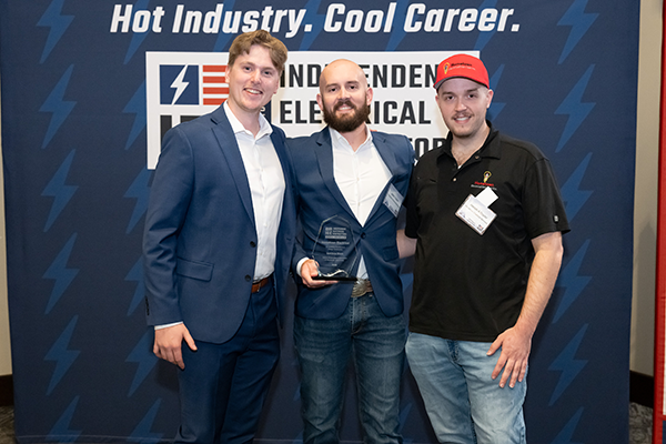 Three men in suits posing with a glass trophy at a career event, in front of a blue backdrop reading 'Hot Industry. Cool Career.'