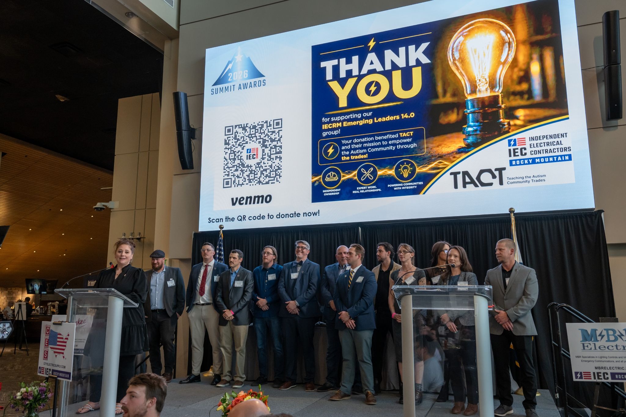 Group of professionals on a stage during a summit/awards ceremony, with a large screen that says 'THANK YOU' and a QR code beside it.