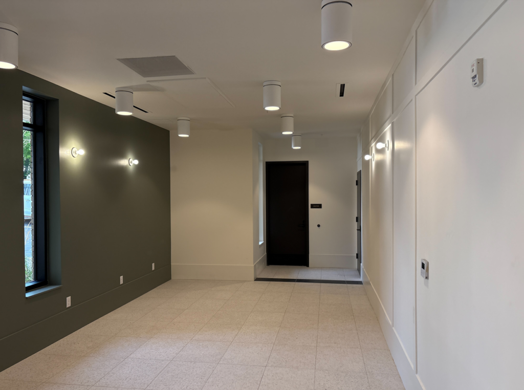 Modern hallway with white walls, dark green left wall, round ceiling lights, and a black door at the far end.