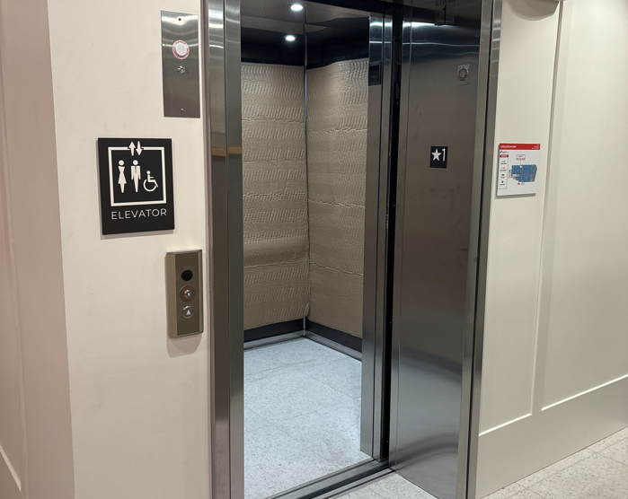 Open elevator doors showing a padded interior and the elevator sign with accessibility icon on the wall outside.